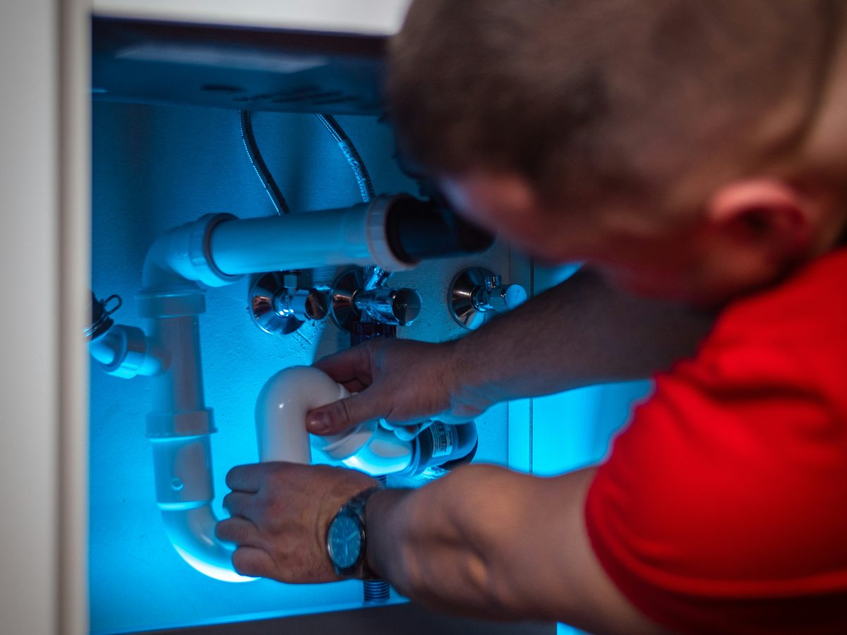 Our plumber working on the drain and shutoff valves beneath a sink