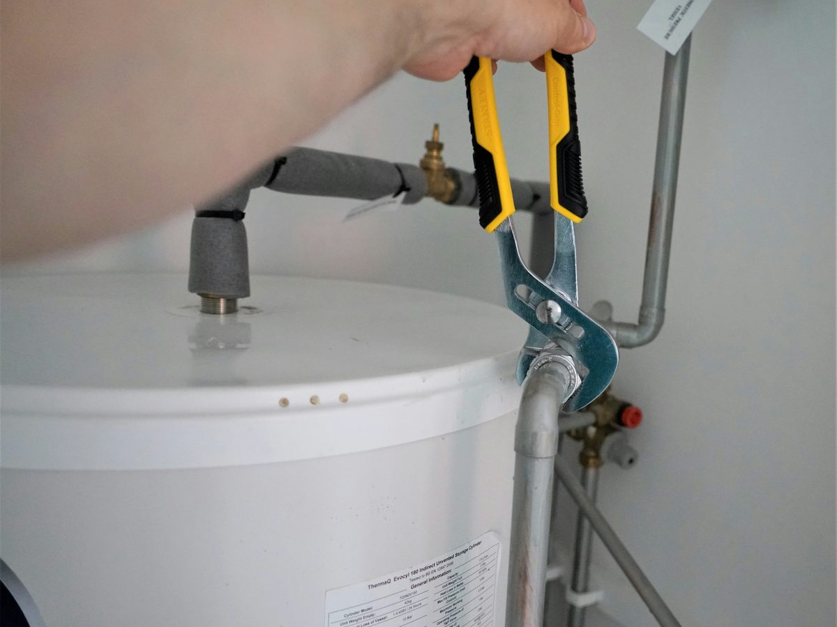 Plumber tightening a fitting on the supply piping above a water heater tank